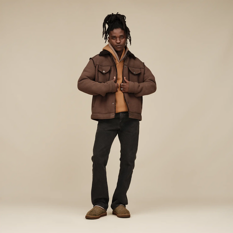 "UGG Tasman Baxter slip-on shoes in brown suede with visible stitching and a cozy lining, lifestyle view worn indoors"