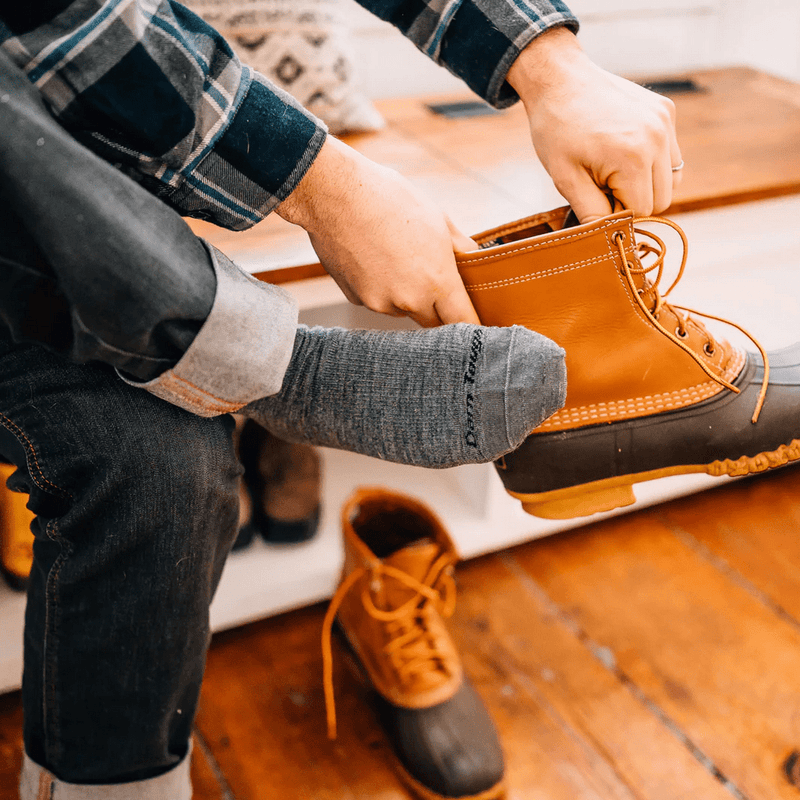 Darn Tough The Standard Mid-Calf Lightweight Lifestyle Socks in gray with durable knit fabric, worn while putting on boots.
