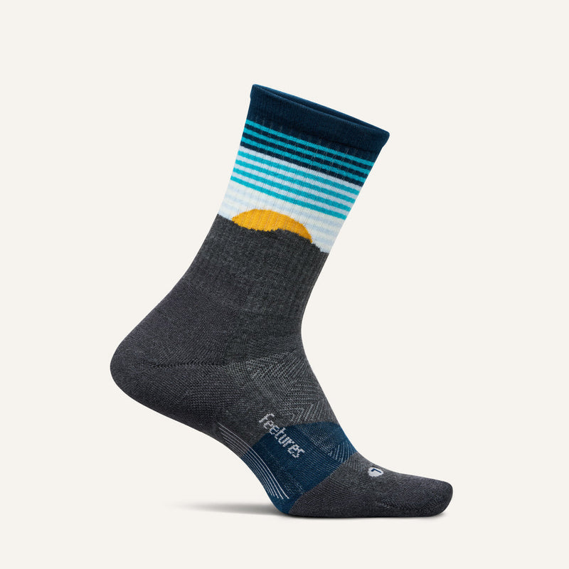 Feetures Trail Max Cushion Mini Crew Sock in dark gray with a sunset design and gradient teal and white stripes, side view.