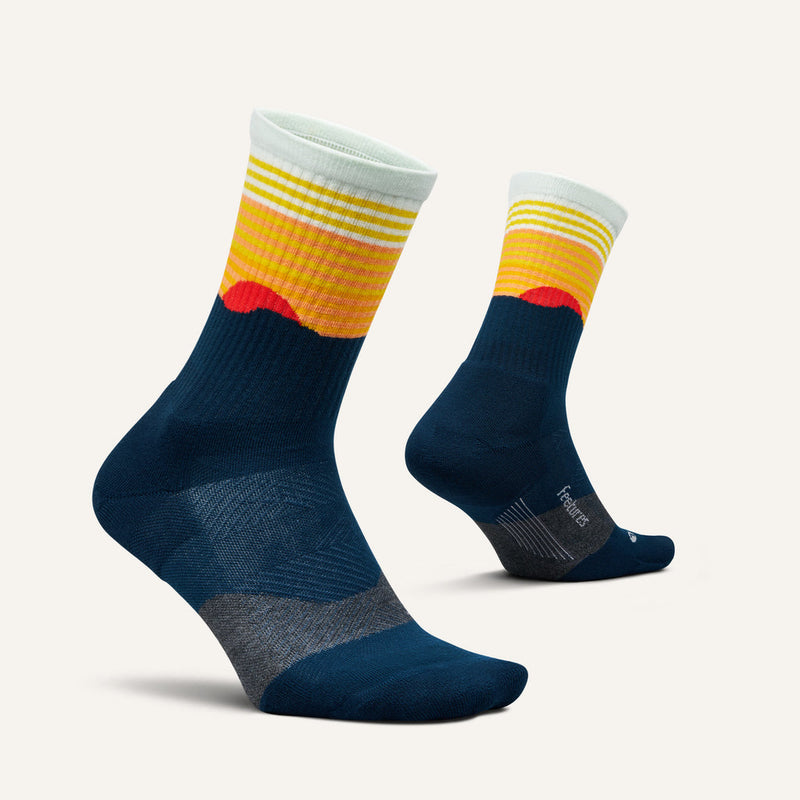 Feetures Trail Max Cushion Mini Crew Socks in navy blue with vibrant yellow and red gradient design, showcasing ribbed cuffs and reinforced heel and toe, side view.